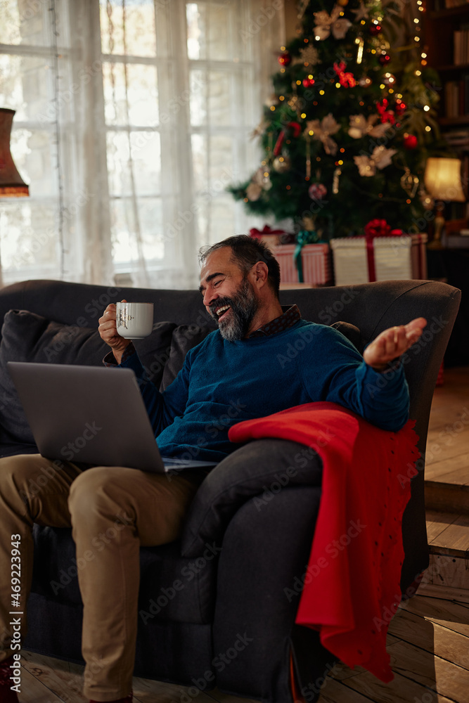 Man using laptop on sofa with Christmas tree in background Man using laptop on sofa with Christmas tree in background