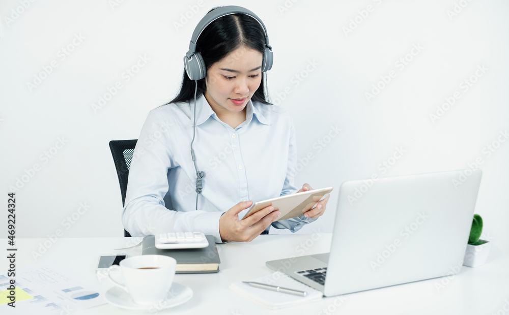 Video call, a young Asian woman wearing headphones, communicates via online video long distance, looking at the digital laptop screen, happily greeted with a friend Video call, a young Asian woman wearing headphones, communicates via online video long distance, looking at the digital laptop screen, happily greeted with a friend
