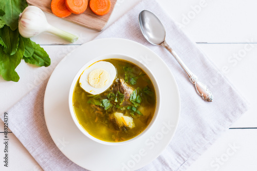 a soup plate with fragrant sorrel soup and boiled egg. ingredients for cooking-sorrel leaves, garlic head, carrot slices. top view.