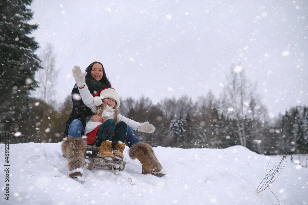 Obraz premium A winter fairy tale, a young mother and her daughter ride a sled in the forest. A girl on a sled with gifts on the eve of the new year in the park.
