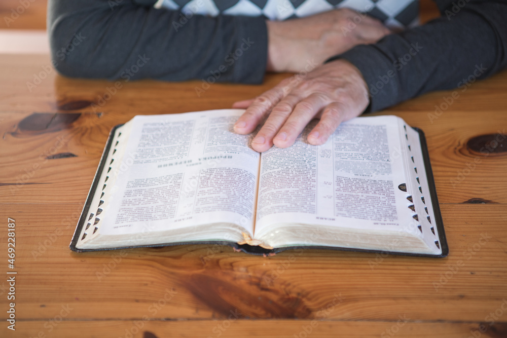 Fototapeta premium senior man praying, reading an old Bible. Hands folded in prayer on a Holy Bible in church concept for faith, spirituality and religion