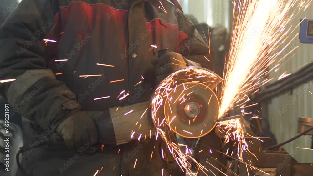 A worker saws metal with an angle grinder, fiery sparks fly