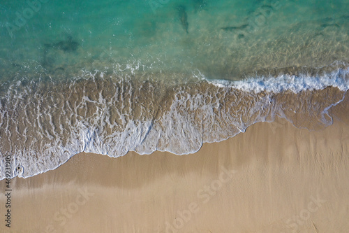 Aerial drone view in abstract mode of waves crashing along the shoreline of a white sand beach with turquoise clear lagoon water.