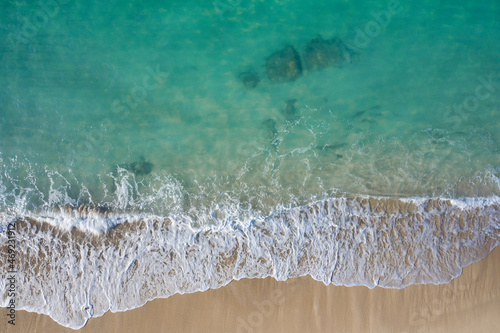Aerial drone view in abstract mode of waves crashing along the shoreline of a white sand beach with turquoise clear lagoon water.