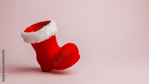 Santa Claus red boot on pastel pink background. Minimal Christmas eve or New Year celebration concept. Elegant winter holidays banner with copy space for text. Advertising or December sale shopping.
