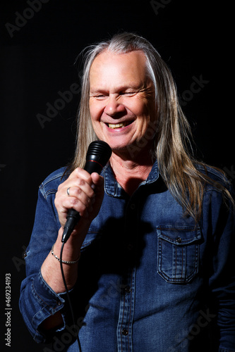 elderly man with long gray hair sings into a microphone