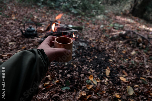 Bushcraft pours water from a bottle into a wood mug.