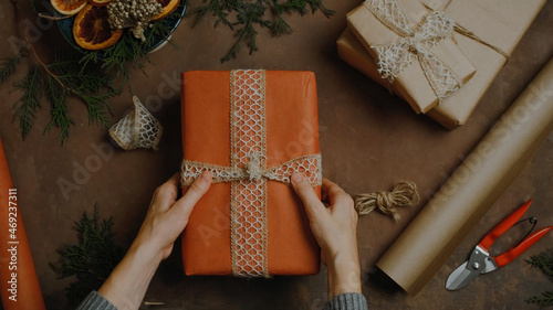 Female hands holding Christmas present wrapped in red kraft paper. DIY Christmas packaging for holiday Christmas gifts. Table top view.