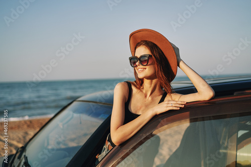 cheerful woman in sunglasses and a hat on the ocean near the car © VICHIZH