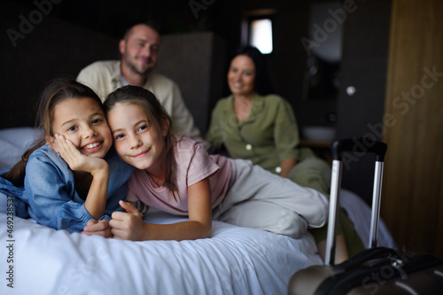 Happy young family with two children sitting on bed and looking at camera at hotel, summer holiday.