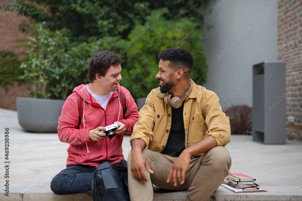 Happy young man with Down syndrome and mentoring friend sitting outdoors