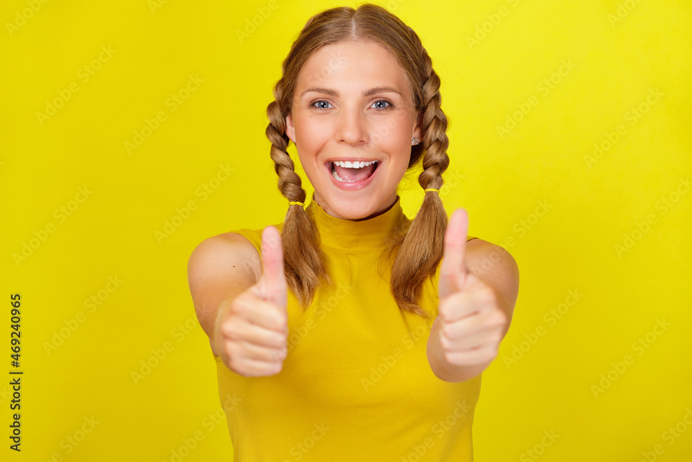 Portrait of happy smiling woman wearing yellow t-shirt showing thumbs up against colored background Portrait of happy smiling woman wearing yellow t-shirt showing thumbs up against colored background
