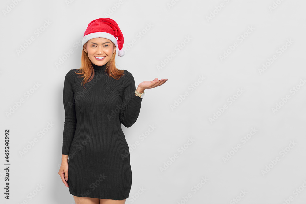 Portrait of smiling young Asian woman in Santa Claus hat showing copy space on palm isolated over white background Portrait of smiling young Asian woman in Santa Claus hat showing copy space on palm isolated over white background
