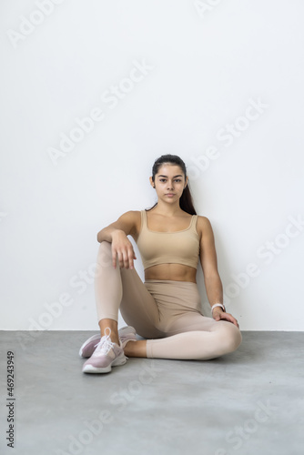 Smiling cheerful attractive beautiful young strong sporty fitness woman doing yoga exercises sitting pointing index fingers on camera stretching on mat floor at home indoor
