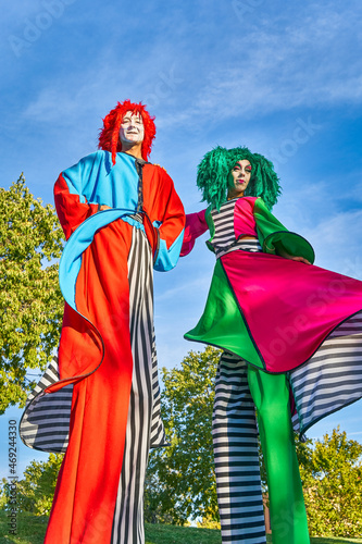 Positive stilt walkers in multicolored costumes standing together in park photo