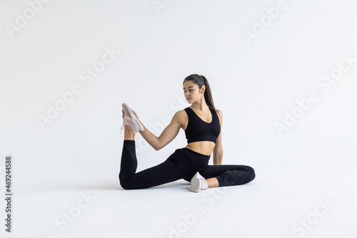 Young sporty attractive woman practicing yoga, doing Mermaid exercise, Eka Pada Rajakapotasana pose, working out, wearing sportswear, pants and top, indoor full length, white yoga studio © F8  \ Suport Ukraine