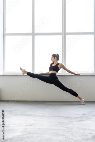 Young attractive yogi woman practicing yoga concept, standing in exercise, handstand pose, working out, wearing sportswear, full length, white loft studio background