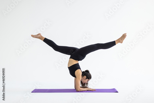 Young woman practicing yoga concept, standing in Adho Mukha Vrksasana exercise, Downward facing Tree pose, working out, wearing sportswear bra and pants, full length