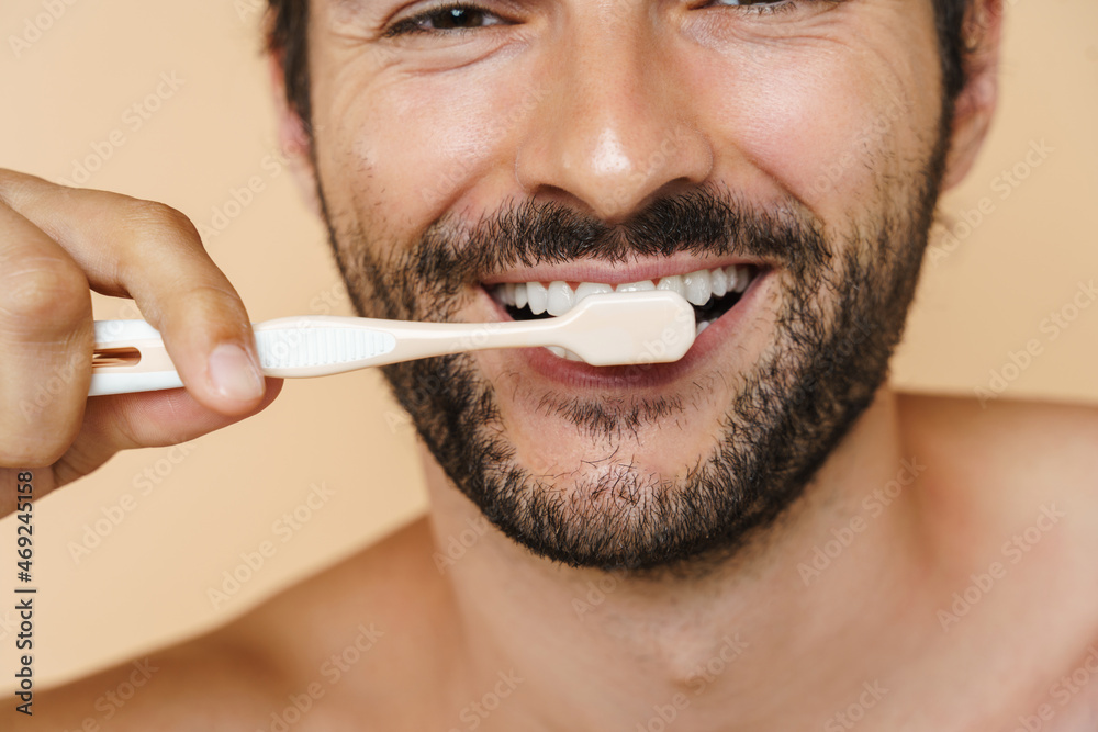 Naklejka premium Young half-naked man smiling while brushing his teeth
