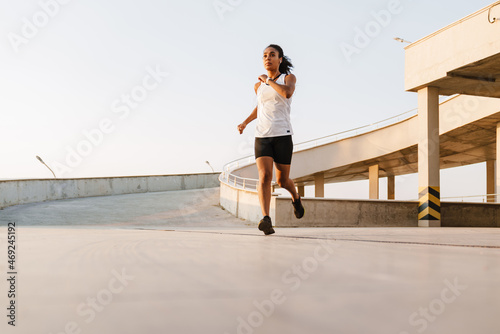 Black sportswoman listening music and running while working out outdoors