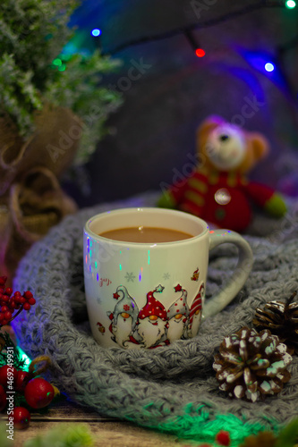 Embrace the holiday warmth with a delightful mug brimming with comfort, set against vibrant baubles, frosted pinecones, and a cheerful plush toy in the backdrop.