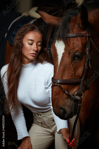 Portrait of smiling female jockey standing by horse in stable © Georgii