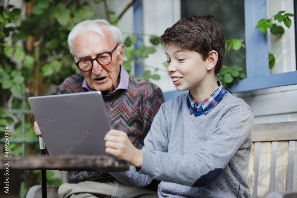 Smiling boy showing laptop to grandfather in backyard Smiling boy showing laptop to grandfather in backyard