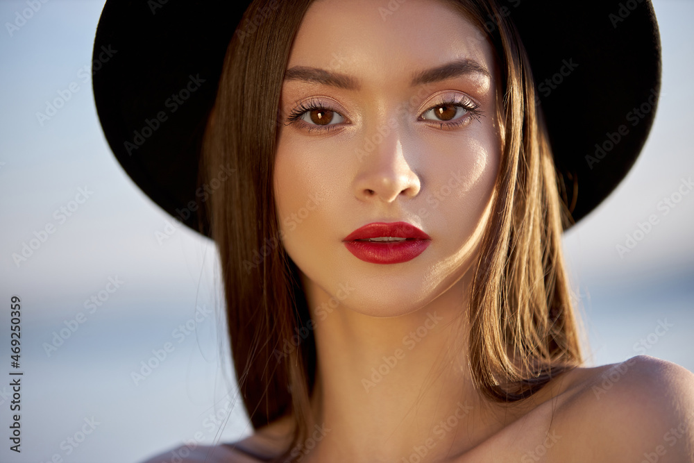 Portrait of a beautiful woman with long hair in a big round black hat. Beauty skin face, bare shoulders. Girl golden light at sunset Portrait of a beautiful woman with long hair in a big round black hat. Beauty skin face, bare shoulders. Girl golden light at sunset