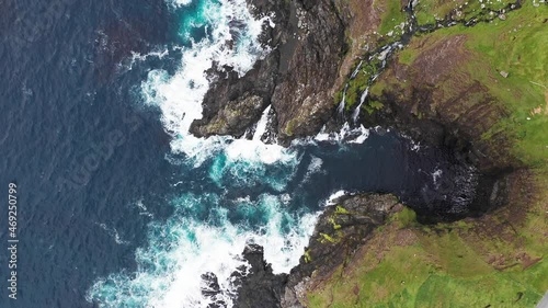 Aerial view of waves break on rocks of Faroe islands cliffs in a blue ocean.Drone Aerial Footage of green nature and the ocean. photo