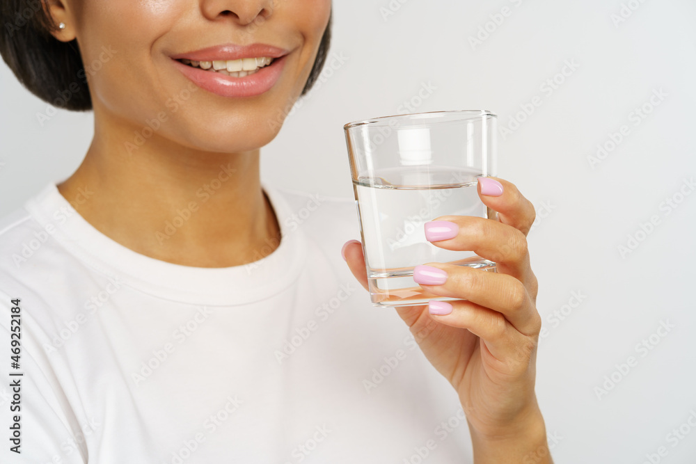 Closeup of smiling african american woman holding glass of water. Female drinking to avoid dehydration, manage weight and care for healthy habits. Water balance and caring for skin and body concept Closeup of smiling african american woman holding glass of water. Female drinking to avoid dehydration, manage weight and care for healthy habits. Water balance and caring for skin and body concept