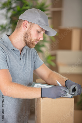 deliveryman leaning on cardboard box to fill in paperwork