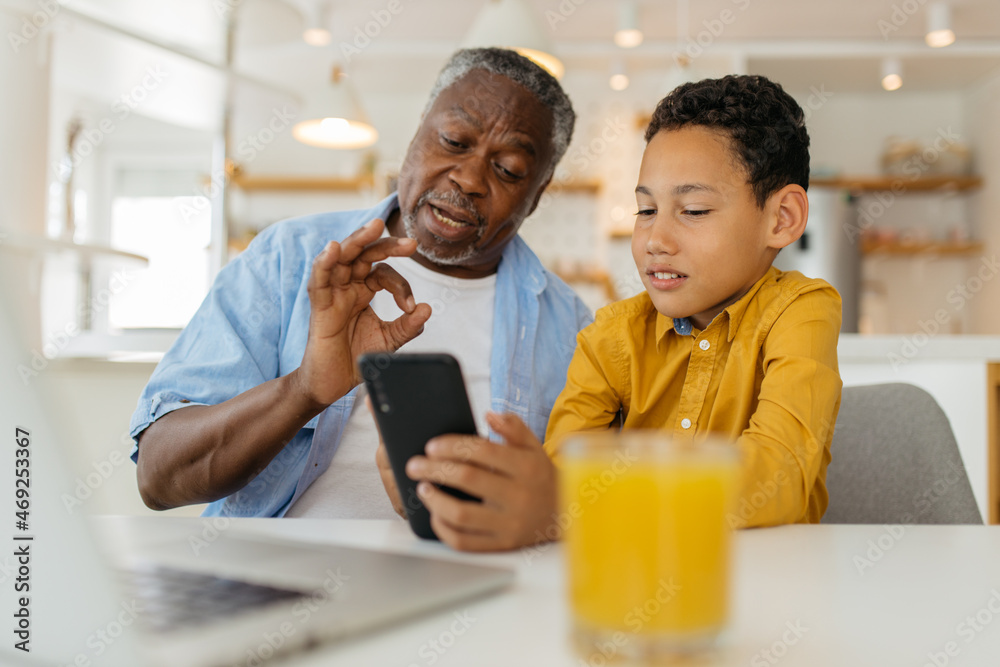 Mixed race grandson showing his grandfather how to use a new phone. He