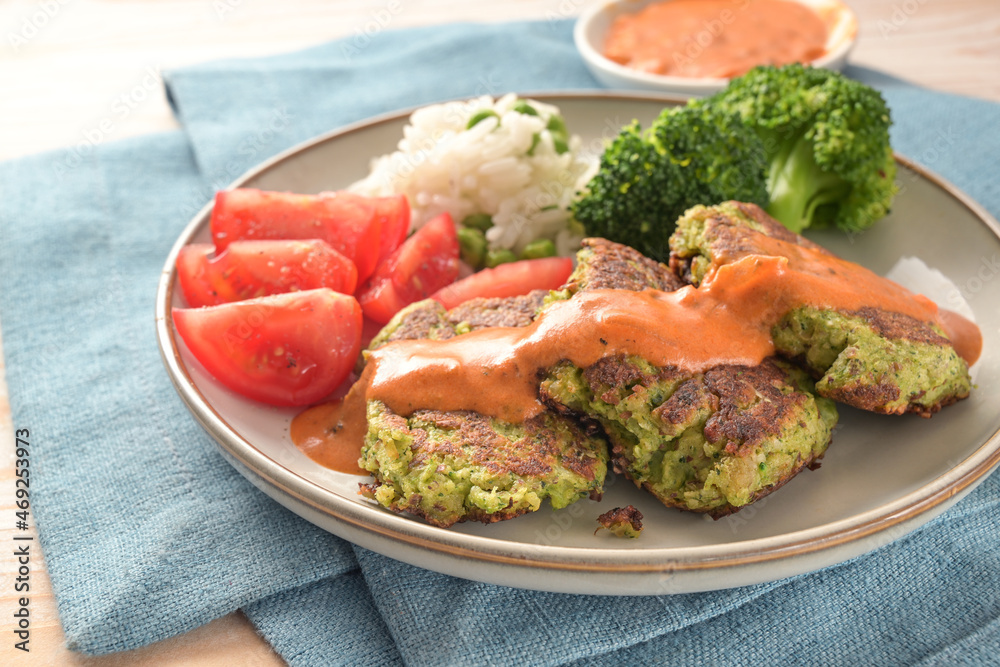Broccoli patties with tomato, rice, vegetables and hot sauce, vegetarian and vegan meal on a blue napkin and a light wooden table, selected focus Broccoli patties with tomato, rice, vegetables and hot sauce, vegetarian and vegan meal on a blue napkin and a light wooden table, selected focus