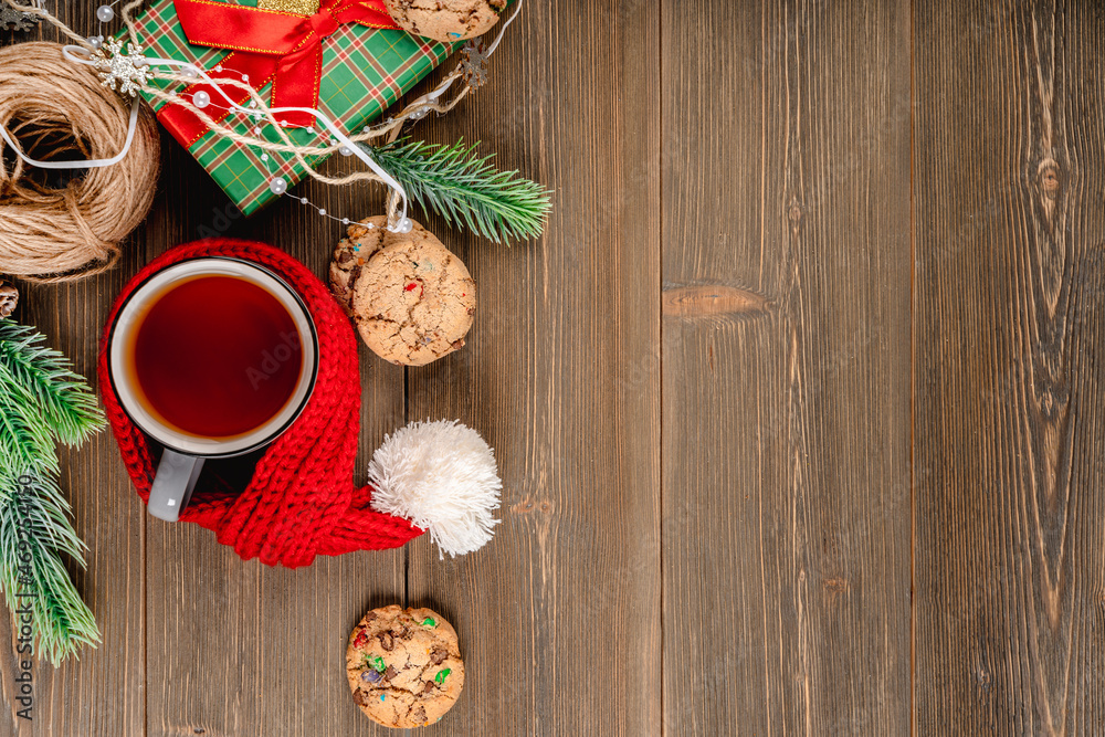A Christmas banner with a place for text with a mug of tea and cookies stands with a red knitted scarf on a wooden table A Christmas banner with a place for text with a mug of tea and cookies stands with a red knitted scarf on a wooden table