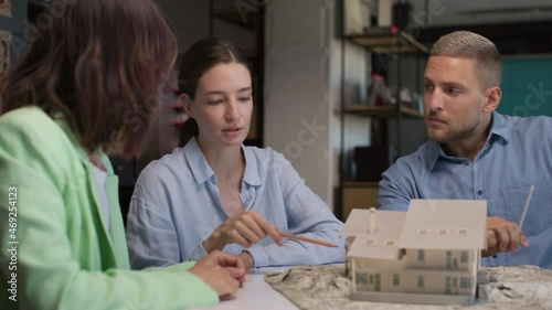 Architects and designer working on house layout in office room. Small group of creative people at desk talks or discussion of home design maquette. Specialists look at detailed prototype of mini model