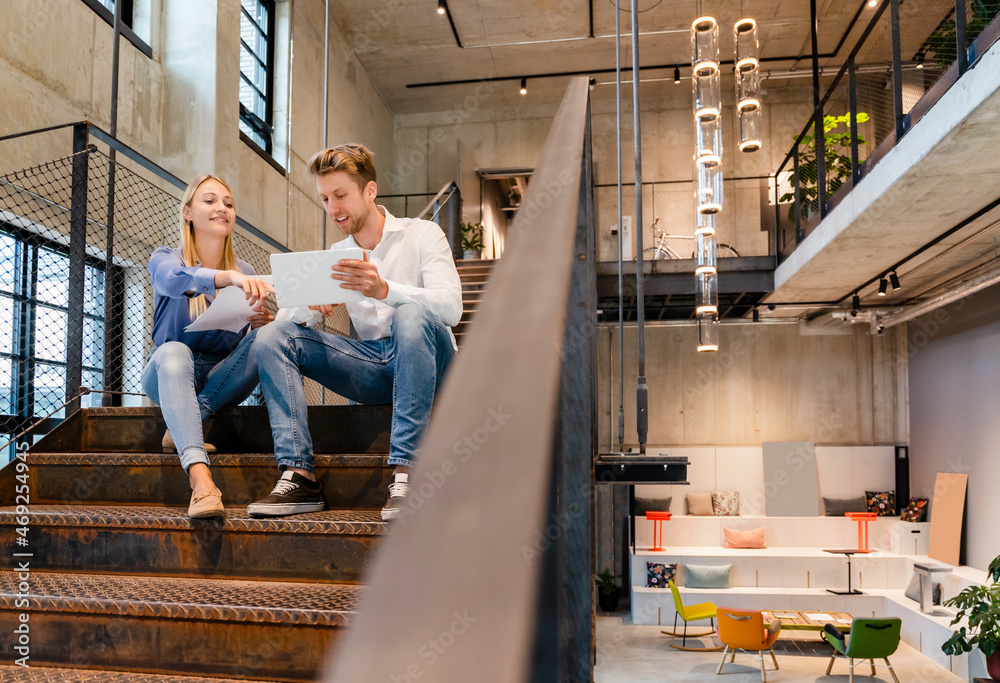Young coworkers discussing over tablet PC on staircase Young coworkers discussing over tablet PC on staircase
