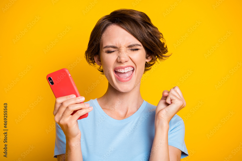 Photo of young girl happy positive smile excited rejoice win victory fists hand hold cellphone isolated over yellow color background Photo of young girl happy positive smile excited rejoice win victory fists hand hold cellphone isolated over yellow color background