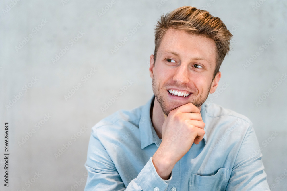 Smiling young businessman with hand on chin in front of wall Smiling young businessman with hand on chin in front of wall