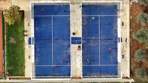 View from above, aerial footage, slow motion video of some people playing on a blue padel court. Padel is a mix between Tennis and Squash. It's usually played in doubles on an enclosed court.