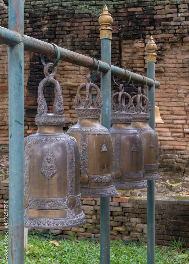 Beautiful traditional buddhist bronze bells hanging in a row with ancient brick stupa in background at historic Wat Umong Maha Thera Chan temple, Chiang Mai, Thailand