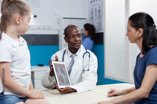 African american radiologist doctor holding tablet computer with heart radiography on screen discussing xray expertise results with mother during examination.Therapist man working in hospital office