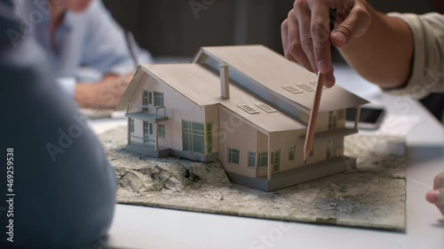 Architects and designers working on house layout in office studio. Group of creative people at desk talks on maquette and discusses home design. Specialists looking at prototype of mini model close-up