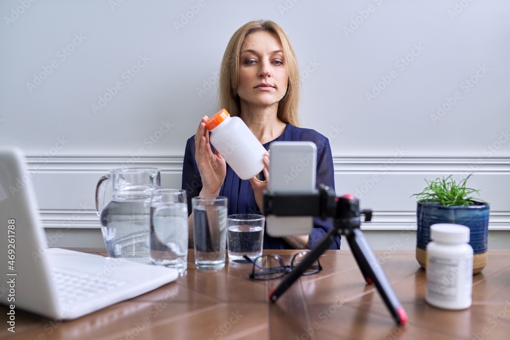 Woman with bottle medicines vitamin supplements telling showing using smartphone, laptop Woman with bottle medicines vitamin supplements telling showing using smartphone, laptop
