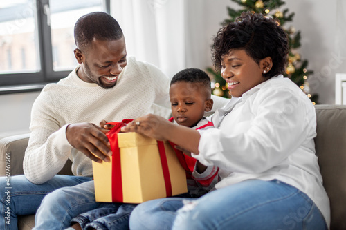family, winter holidays and people concept - happy african american mother, father and baby son opening gift box at home on christmas