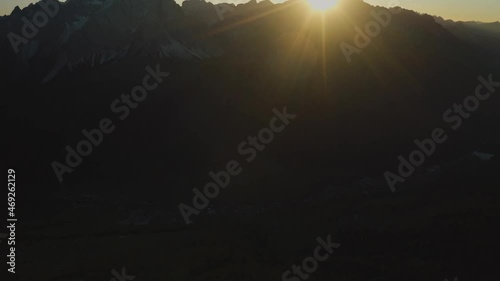 Sunset behind Punta Tre scarperi Peak in Italian Dolomites - Silhouette of mountains and lighting sun hiding in background - Aerial view photo