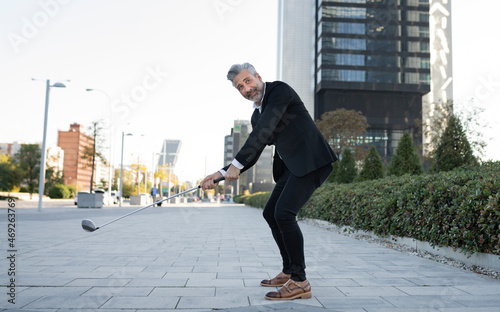 Businessman playing golf on footpath photo
