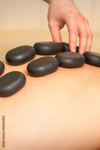 Young caucasian woman receiving back massage with black stones by masseur in spa salon. A woman getting a spa treatment