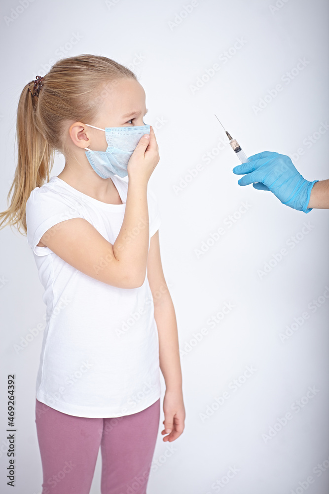 The hands of women in blue gloves with a syringe,in front of a girl in a medical mask
