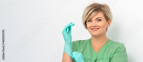 Doctor beautician puts on sterile blue gloves smiling prepares to receive clients on white