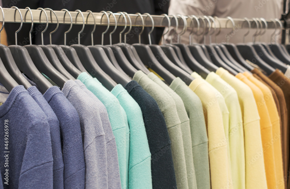 Obraz premium Multicolored woolen knitted sweaters hanging on hangers close-up.